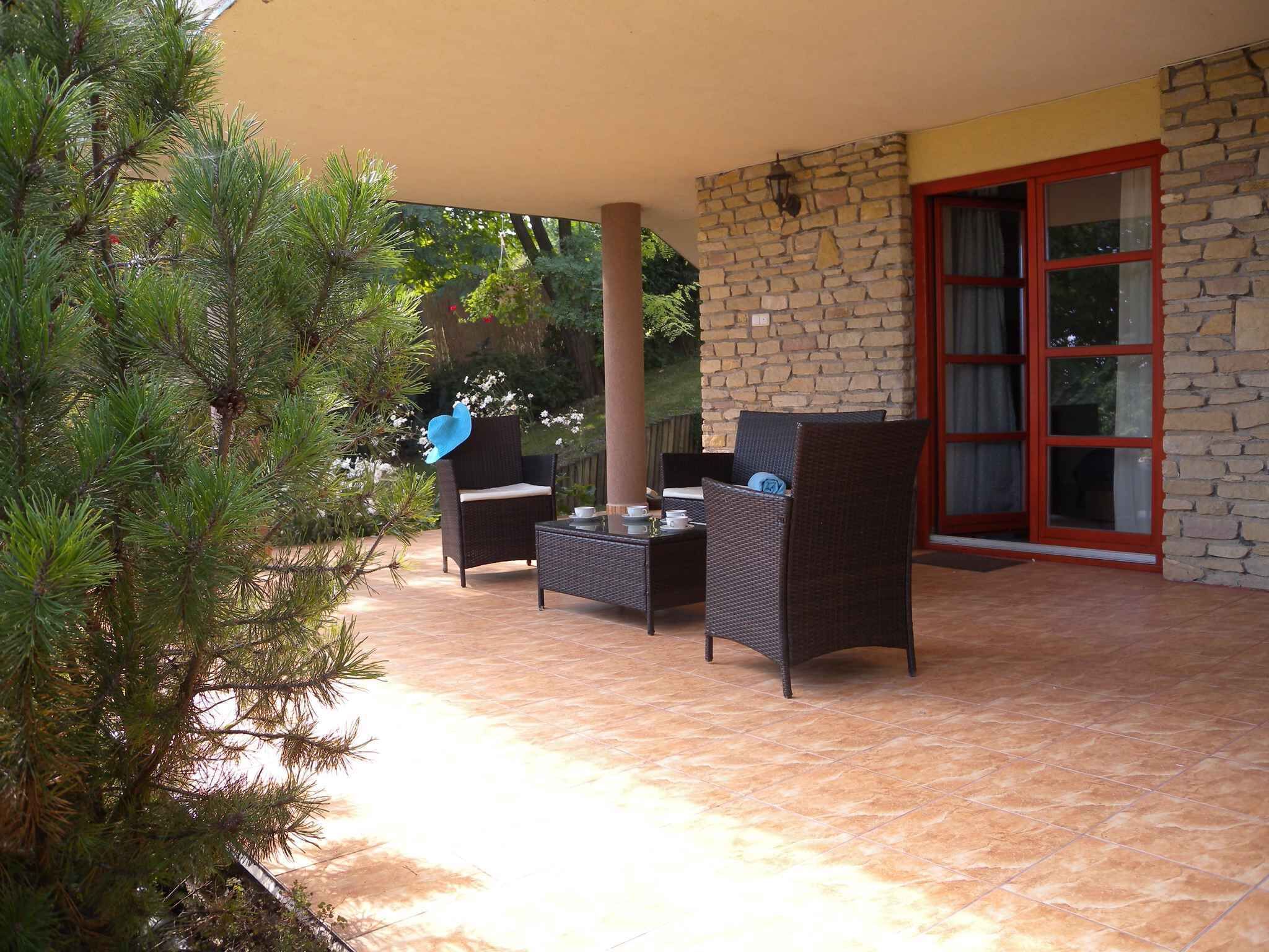 Un patio exterior con mobiliario de mimbre, un muro de piedra y una puerta de cristal.