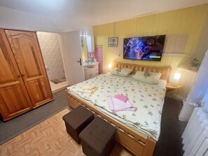 A bedroom with a wooden bed, a TV mounted on the wall, a bedside table with a lamp, and a wardrobe. - Double room - Schulz (Heringsdorf)