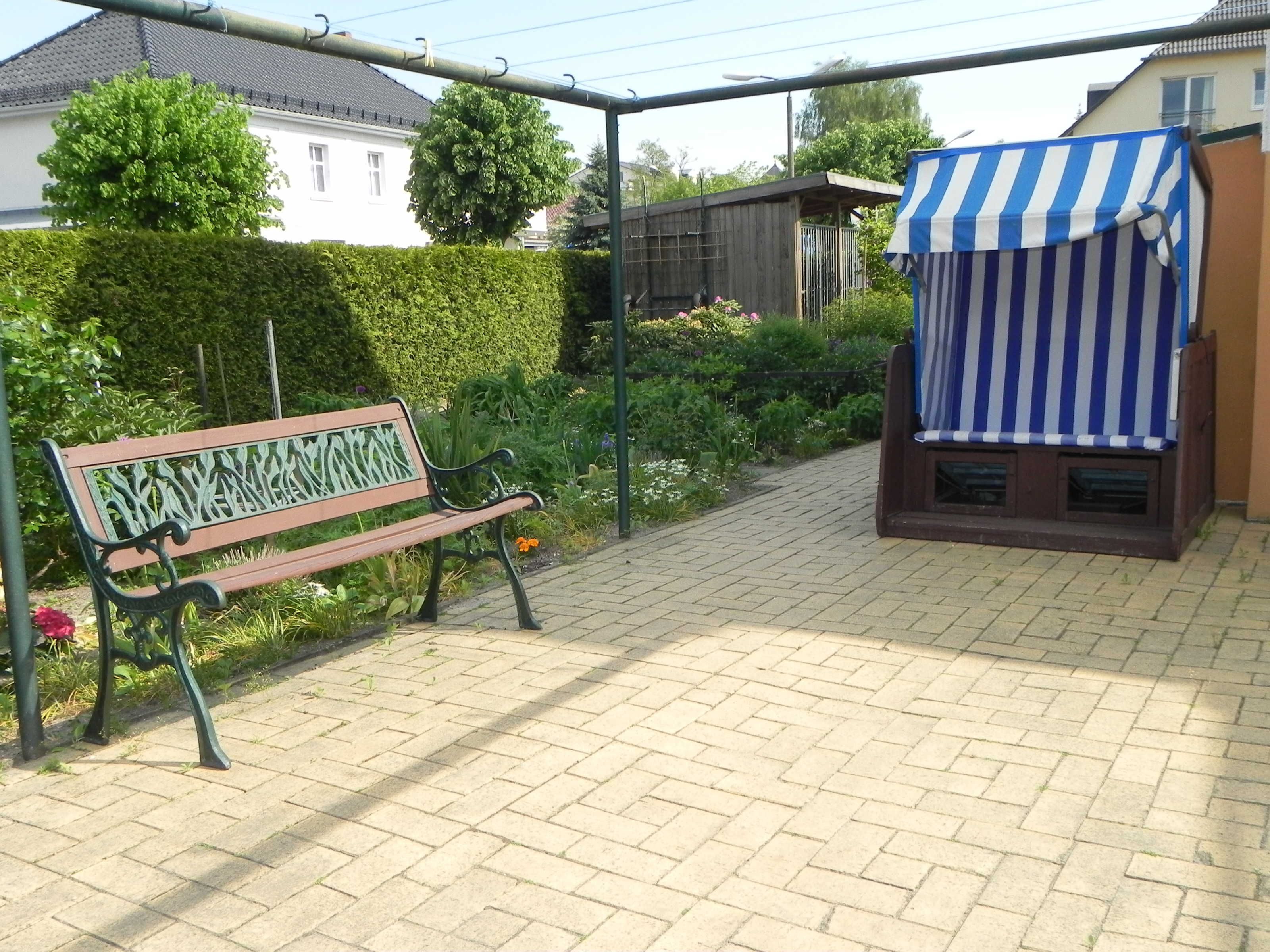 A bench with a metal frame and wooden seat, a striped awning, and a paved walkway.