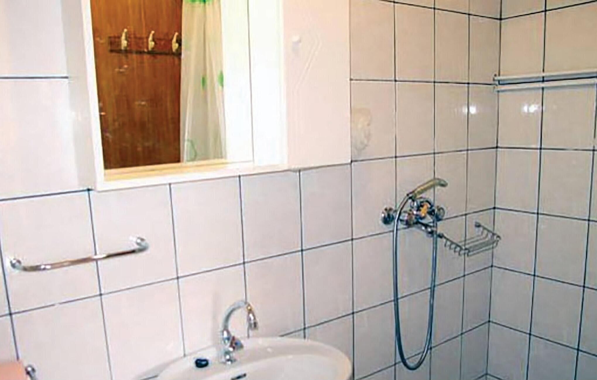 A bathroom with white tiled walls, a sink with a faucet, a shower area with a hose, and a towel rack.