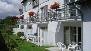 A white building with balconies, a white fence, and outdoor seating.