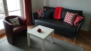 Een woonkamer met een zwarte bank, rode en witte kussens, een rode plaid, een witte salontafel en een rode decoratie.