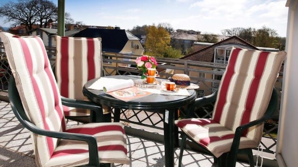 Een terras met gestreepte stoelen en een tafel, een vaas met bloemen en een glas bier.