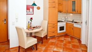 Een compacte keuken met houten kastjes, een eettafel met stoelen en een betegelde vloer.