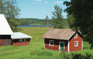 A rural setting with two red wooden houses, one with a white roof and another with a green door, surrounded by lush greenery and a lake in the background. - Stunning home in Vrigstad with WiFi (Vrigstad)