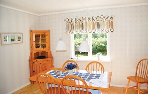 A dining area with a wooden table, four chairs, a cabinet with glass doors, and a window with curtains. - Stunning home in Vrigstad with WiFi (Vrigstad)