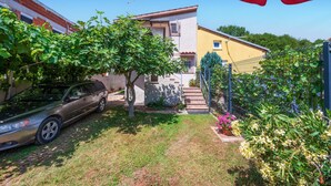 A residential area with a parked car, a staircase leading to a house, and a garden with various plants and flowers.
