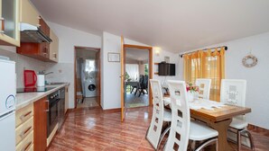 A compact kitchen with a washing machine, a dining area with a table and chairs, and a TV mounted on the wall.