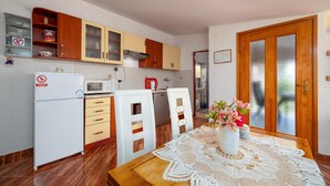 A compact kitchen with wooden cabinets, a white refrigerator, a microwave, and a sink. There's a dining table with a lace tablecloth and a vase of flowers.