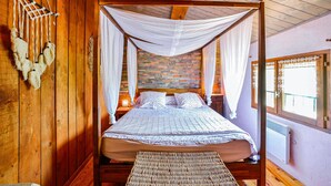 Ein Zimmer mit Holzboden, einem Bett unter einem Baldachin, einer Ziegelwand und einem Fenster mit Vorhängen.