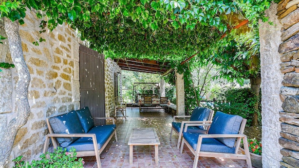 Eine Terrasse im Freien mit Steinmauern, zwei blauen Sitzgelegenheiten mit Polstern, einem Holztisch und einer Holzschaukel.