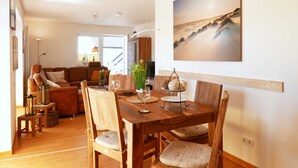 Un coin repas avec une table et des chaises en bois, un vase contenant des plantes vertes et un tableau accroché au mur représentant une scène de plage.