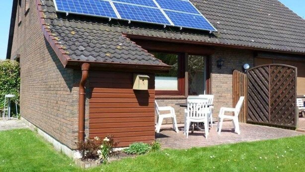 A house with solar panels on the roof, a brick exterior, and a small patio with chairs.