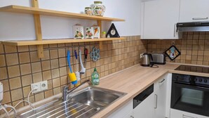 A kitchen with a stainless steel sink, wooden countertop, white cabinets, a stove, and a toaster.