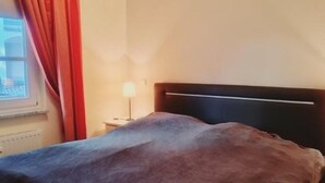 Een bed met hoofdbord, een raam met gordijnen en een bedlamp.