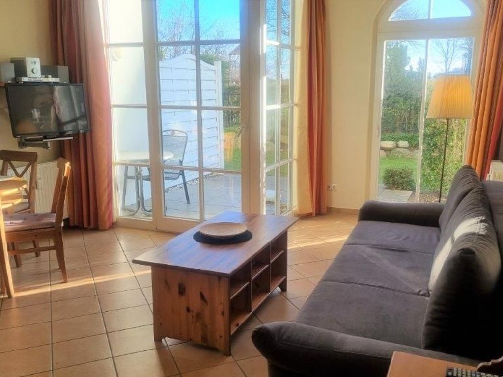 Uma sala de estar com sofá, mesa de centro de madeira, televisão e uma grande porta de vidro deslizante para área externa.