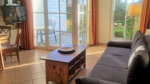 Een woonkamer met een bank, een houten salontafel, een televisie en een grote glazen schuifdeur die leidt naar een buitenruimte.