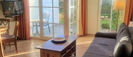 Uma sala de estar com sofá, mesa de centro de madeira, televisão e uma grande porta de vidro deslizante para área externa.