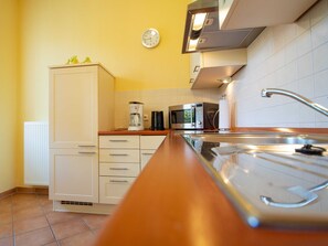 Una cocina con alacenas blancas, una cafetera, un microondas y un lavamanos de acero inoxidable.