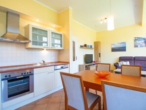 Cocina compacta con armarios blancos, horno integrado y comedor con mesa y sillas de madera.
