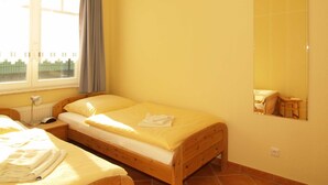 Quarto com duas camas de solteiro, janela com cortinas, radiador e espelho na parede.