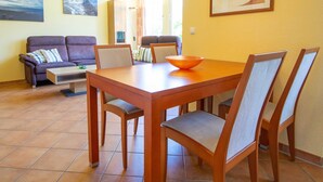 Uma sala de jantar com uma mesa e cadeiras de madeira, uma tigela sobre a mesa e um sofá ao fundo.