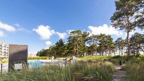 A pool area with lounge chairs, surrounded by tall trees and a clear sky. - Beach front apartment in Binz with WiFi (Prora/Rügen)
