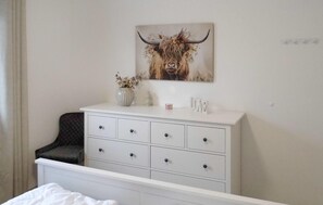 A bedroom with a white dresser, a small vase with flowers, and a painting of a bull on the wall. - Ferienhaus 15 in Kirchheim (Kirchheim)