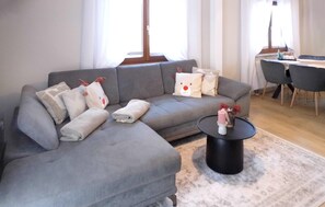 A modern living room with a grey sofa, decorative pillows, a small black coffee table, and a dining area with a chair and table. - Ferienhaus 15 in Kirchheim (Kirchheim)
