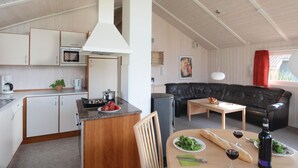 Un espacio habitable compacto con kitchenette, comedor y zona de estar con sofá y mesa.