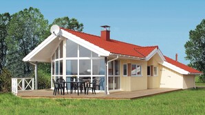 Una casa de dos pisos con techo rojo, ventanas grandes y una terraza de madera.