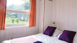 Un dormitorio con una cama, dos almohadas moradas, una ventana con cortinas y un armario.