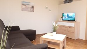 A living room with a sofa, a coffee table, a TV, and a cabinet. - (282) 2-room apartment-Hafenstraße - Apartment complex Yachthafenresidenz (Kühlungsborn)