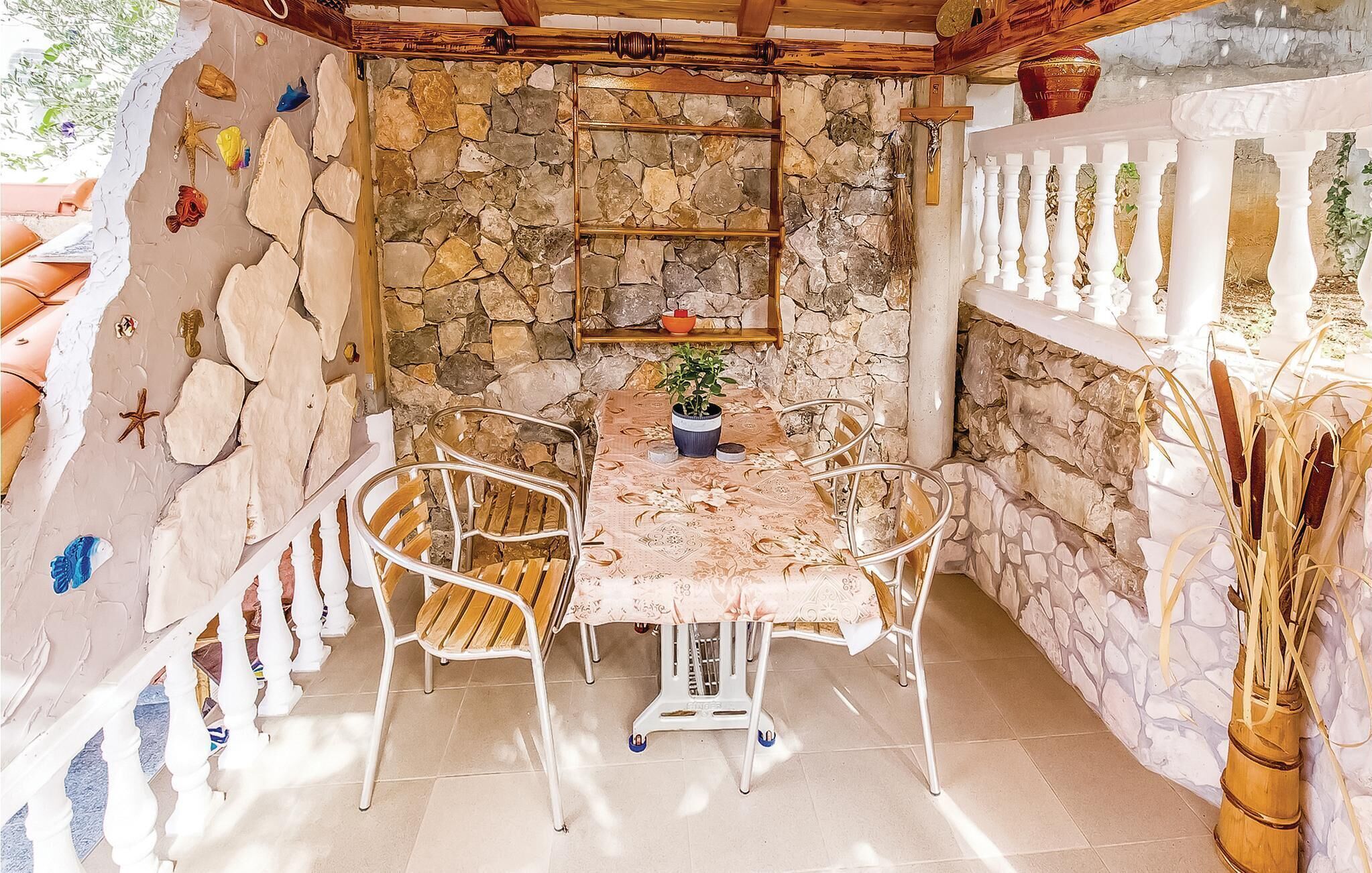 Eine Terrasse mit Steinwänden, einem Tisch, Stühlen, einem Blumentopf und einer rustikalen Holzbalkendecke.