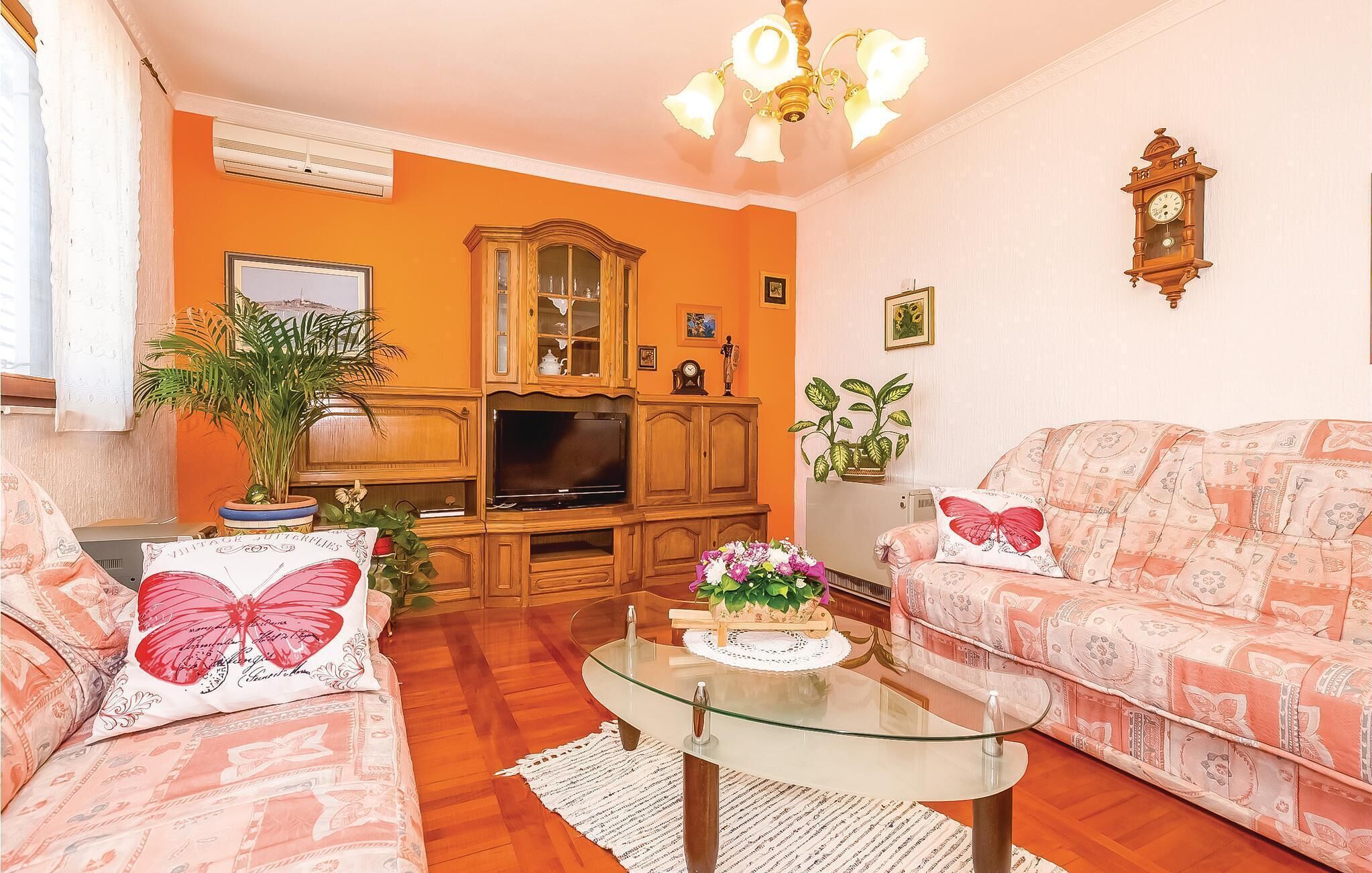 Una sala de estar con un sofá, una mesa de centro de vidrio, un televisor y un mueble de madera.