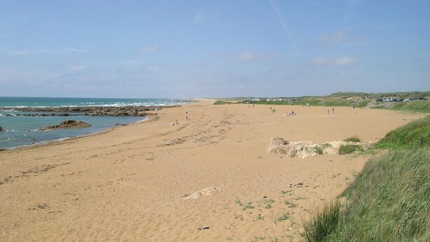Ein weiter Sandstrand mit Felsen und einem klaren Himmel.