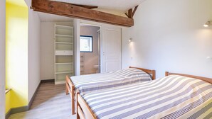 Ein Schlafzimmer mit zwei Holzbetten, einem eingebauten Kleiderschrank, einer Duschkabine und einem Fenster mit Tageslicht.