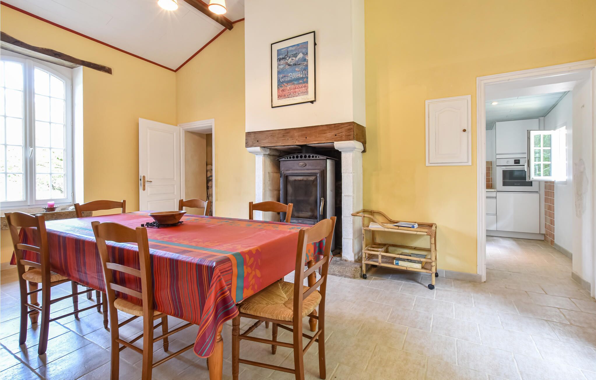 Un'area pranzo con un tavolo imbandito per quattro persone, una sedia in legno, un caminetto e una cucina sullo sfondo.