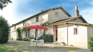 Ein zweistöckiges Gebäude mit Garten, einschließlich Tisch und Stühlen unter einem roten Sonnenschirm.