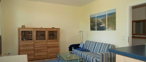 Un salon avec un canapé, une table basse en verre, un meuble en bois et un tableau accroché au mur.