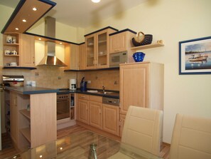 Una cocina moderna con armarios de madera, una isla central y un comedor con mesa y sillas de vidrio.