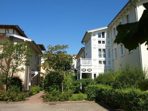 Ett bostadsområde med en asfalterad gångväg, välväxta träd och flerfamiljshus med balkonger.