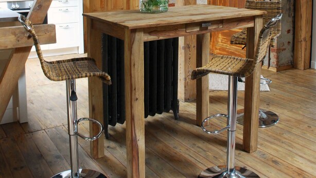 Een landelijke keuken met zichtbare houten balken, een bakstenen muur en een houten tafel met twee barstoelen.