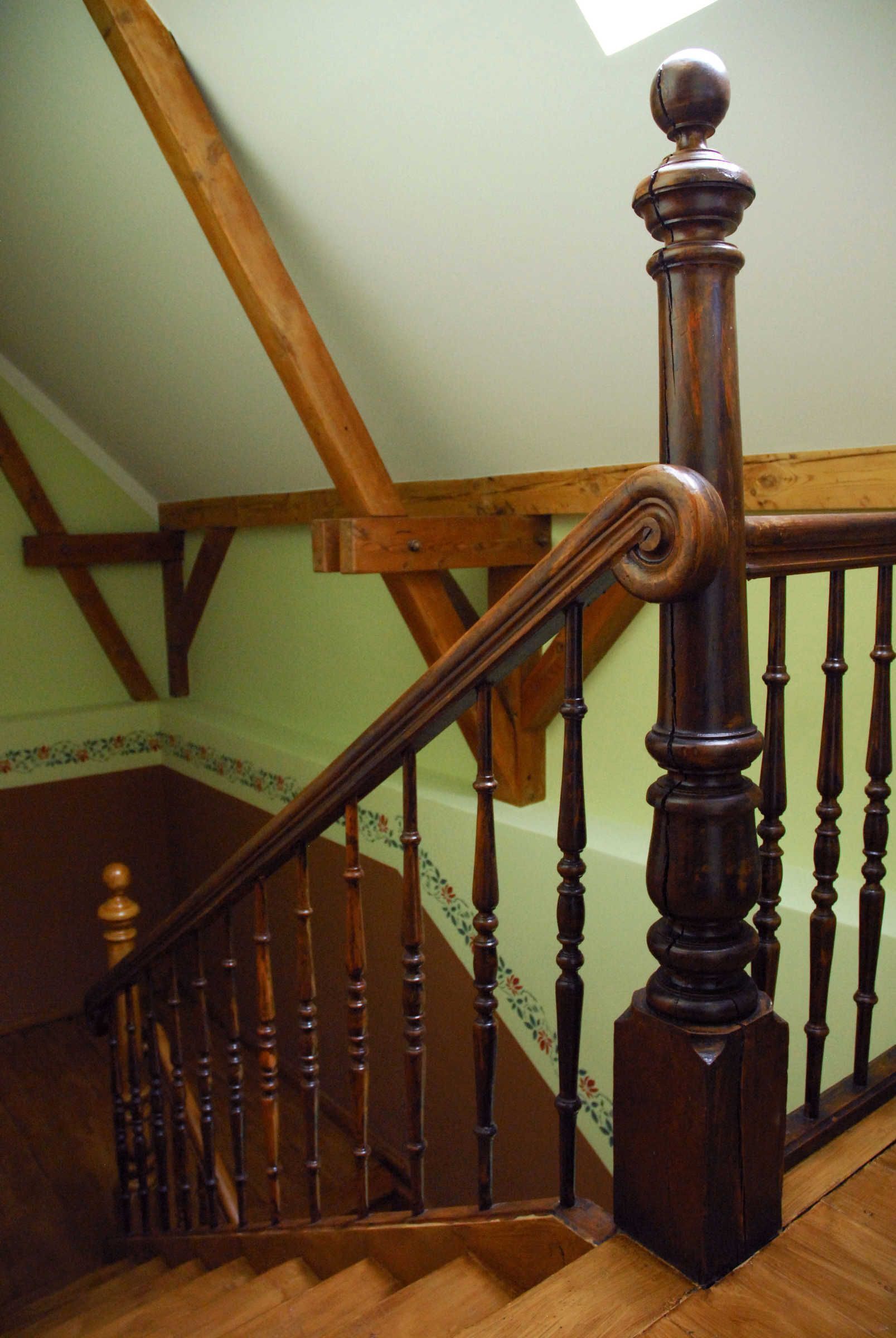 A wooden staircase with a balustrade, a wooden handrail, and a wooden post at the top.