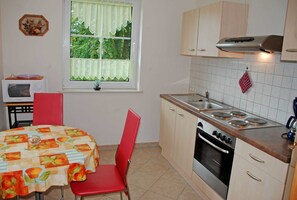 A compact kitchen with a dining table, chairs, a microwave, an oven, and a window with curtains. - Apartment Lisa with terrace on the coastal forest (Sellin)