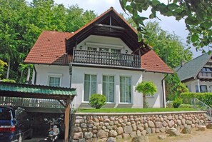 A two-story house with a stone wall in front, a balcony, and a covered porch. - Apartment Lisa with terrace on the coastal forest (Sellin)
