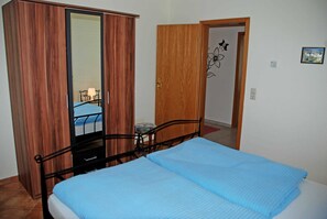 A bedroom with a bed, a wardrobe, a mirror, and a door leading to another room. - Apartment Lisa with terrace on the coastal forest (Sellin)