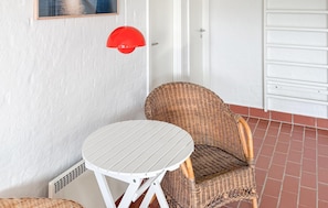 Un juego de mesa blanca y silla de mimbre frente a una pared blanca con una lámpara colgante roja.