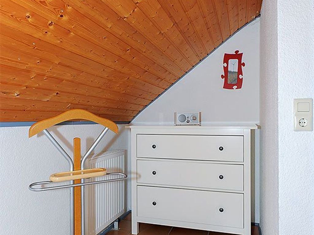 Een kamer met een houten plafond, een witte ladekast, een radiator en een houten kapstok.
