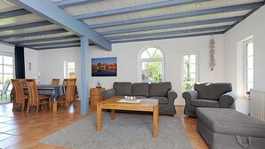 Un salon spacieux avec un plafond haut, un coin repas avec des meubles en bois et un ensemble de canapés gris.